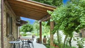 Eine überdachte Terrasse mit Steinböden, Sitzgelegenheiten im Freien und Blumentöpfen.