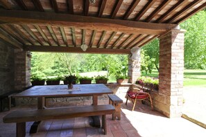An outdoor patio with a wooden table and benches, surrounded by potted plants and a brick wall.