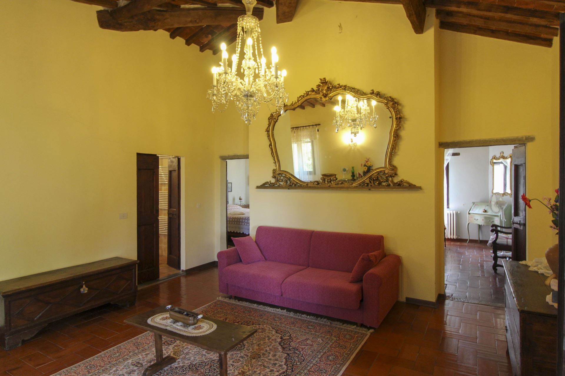 Uma sala de estar ampla com um lustre grande, um sofá roxo e um espelho com moldura decorada.