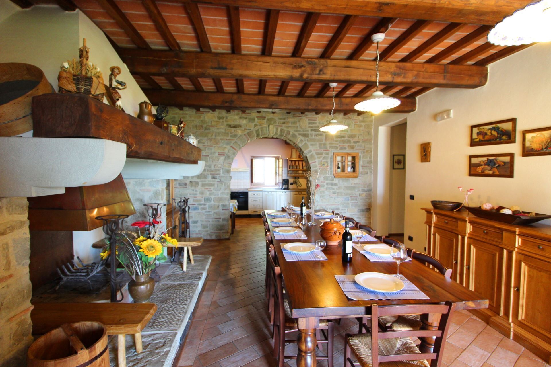 Un comedor rústico con una larga mesa de madera dispuesta para una comida, paredes de piedra y vigas de madera en el techo.