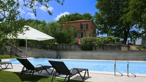 A swimming pool with lounge chairs, a white umbrella, and a brick house in the background.