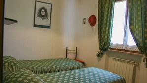 A bedroom with two single beds, a window with curtains, a radiator, and a framed picture on the wall.