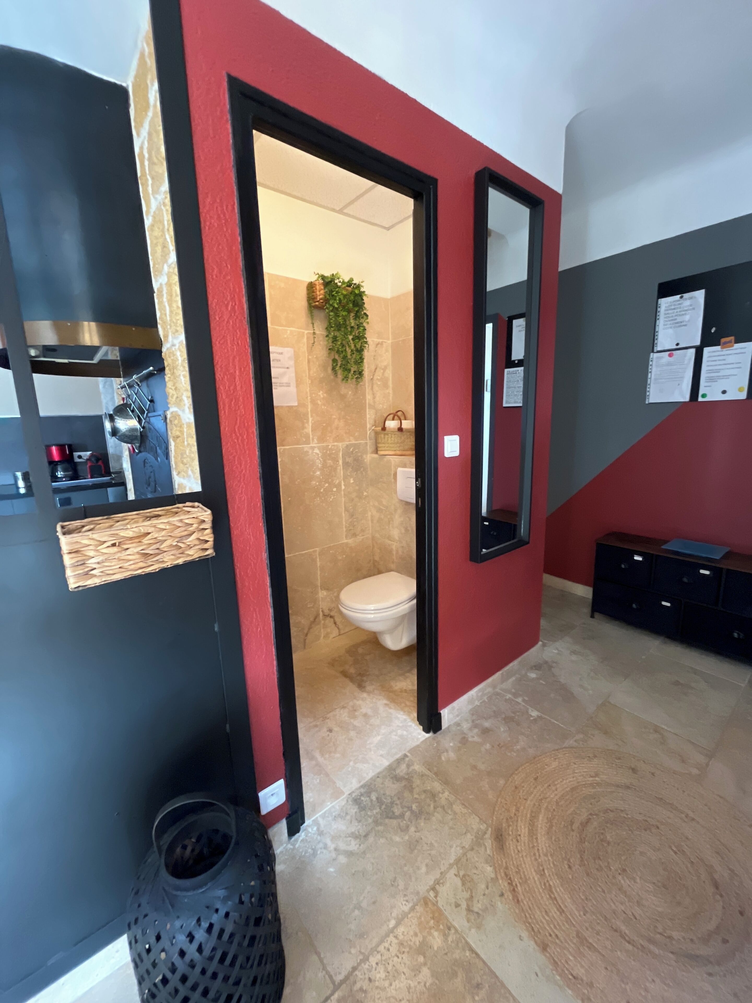 A modern bathroom with a red accent wall, a mirror, a toilet, and a sink area.