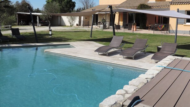 A swimming pool with lounge chairs, a covered patio area, and a building with a tiled roof.