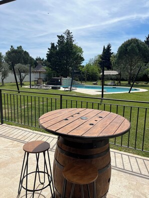 A wooden table with a barrel stool, a pool, and a gazebo in the background.