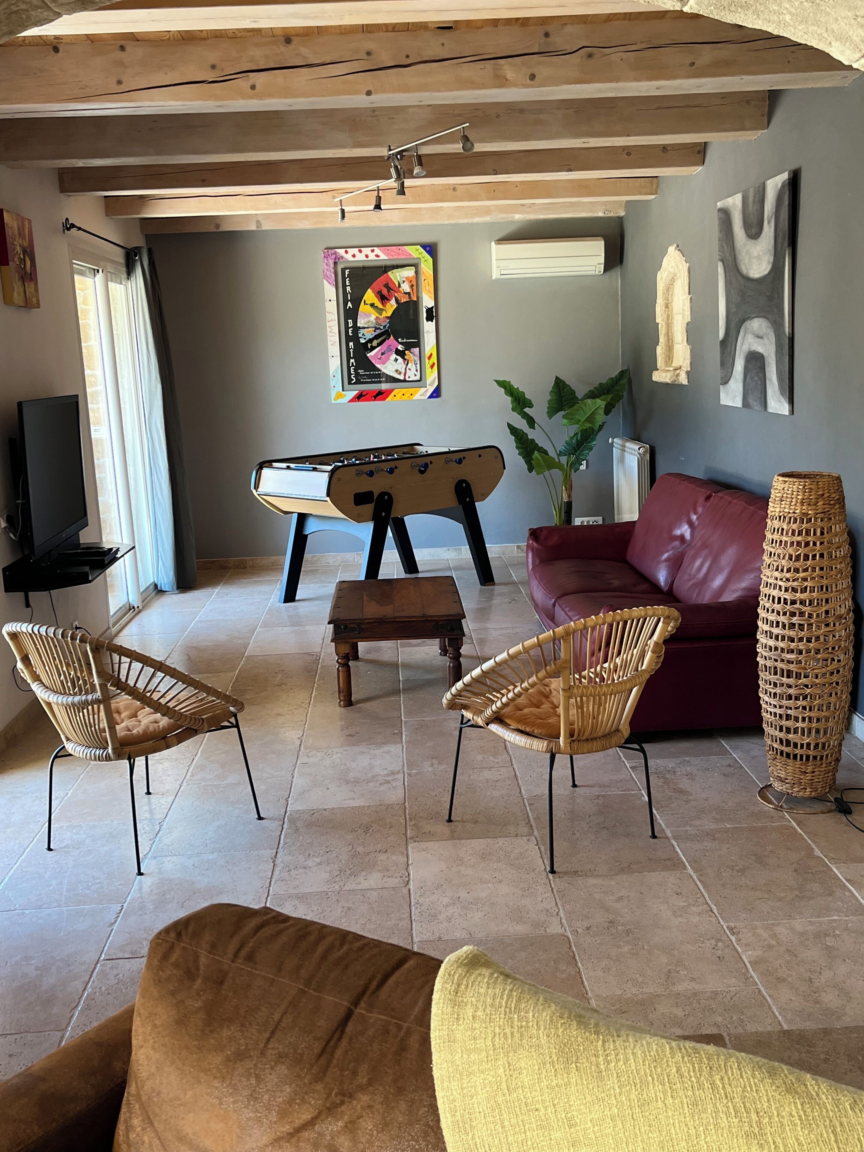 A living room with a sofa, two wicker chairs, a coffee table, a foosball table, and a television.