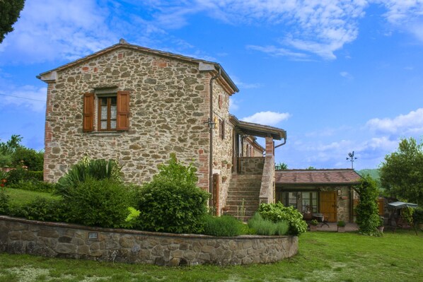 A stone building with a wooden window and a door, surrounded by greenery.