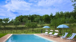 Une piscine entourée d’une terrasse en briques et d’une clôture en bois, avec des chaises longues et des parasols.
