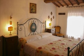A bedroom with a bed, two bedside tables, a chair, a wall-mounted picture, and a window with curtains.