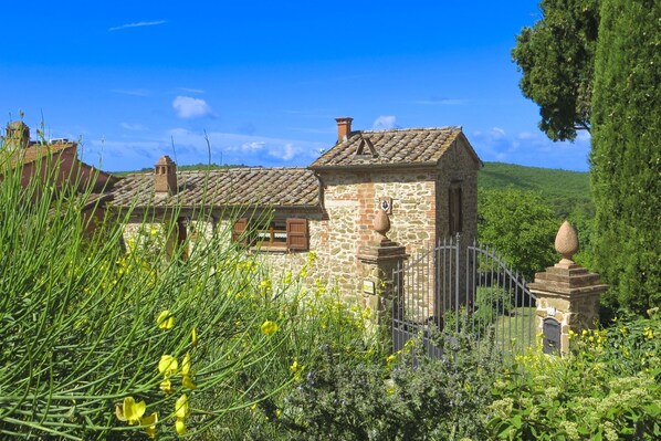 A stone building with a tiled roof, surrounded by greenery and a clear blue sky.
