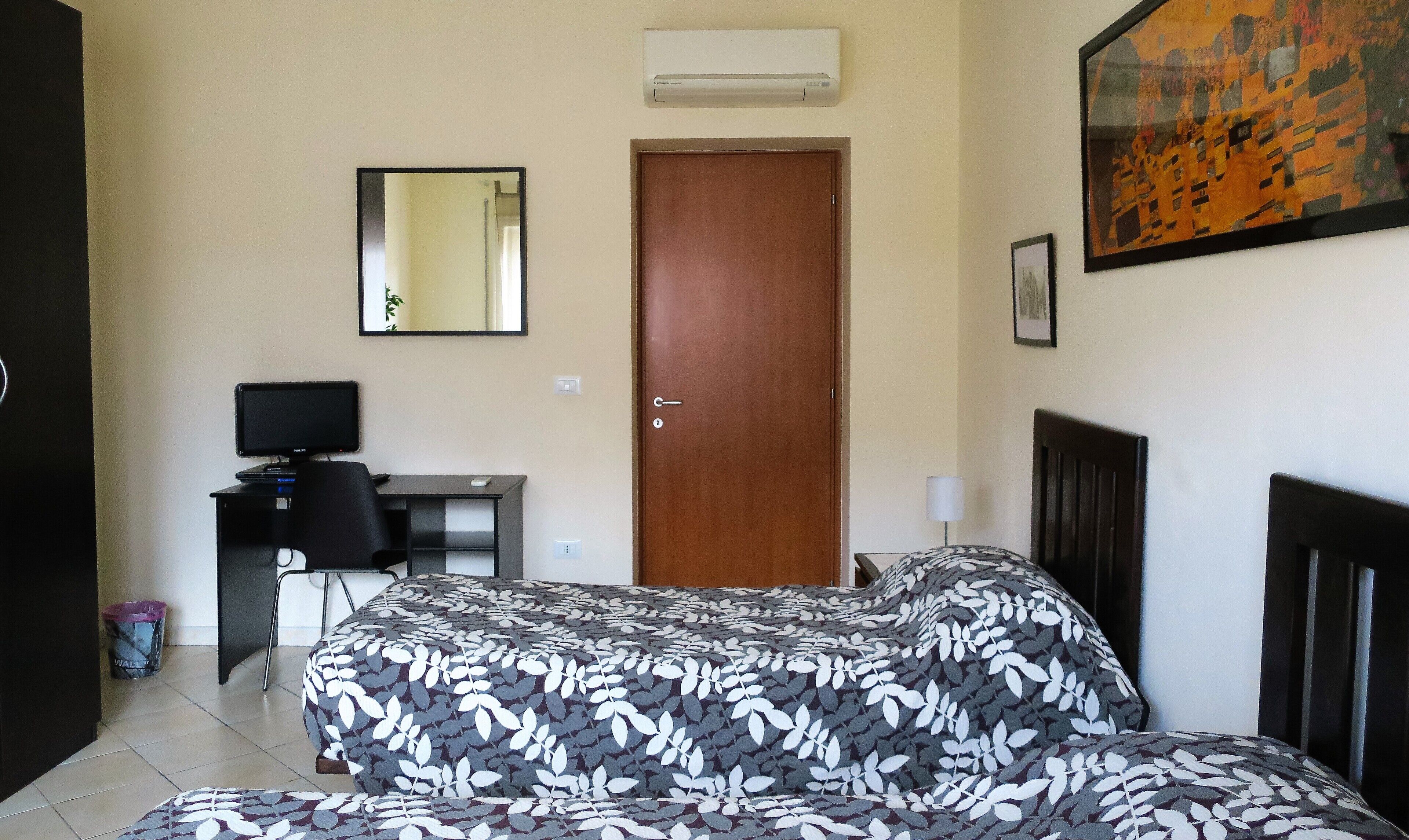 Une chambre d’hôtel avec un lit, un bureau avec un ordinateur, une porte et un tableau au mur.