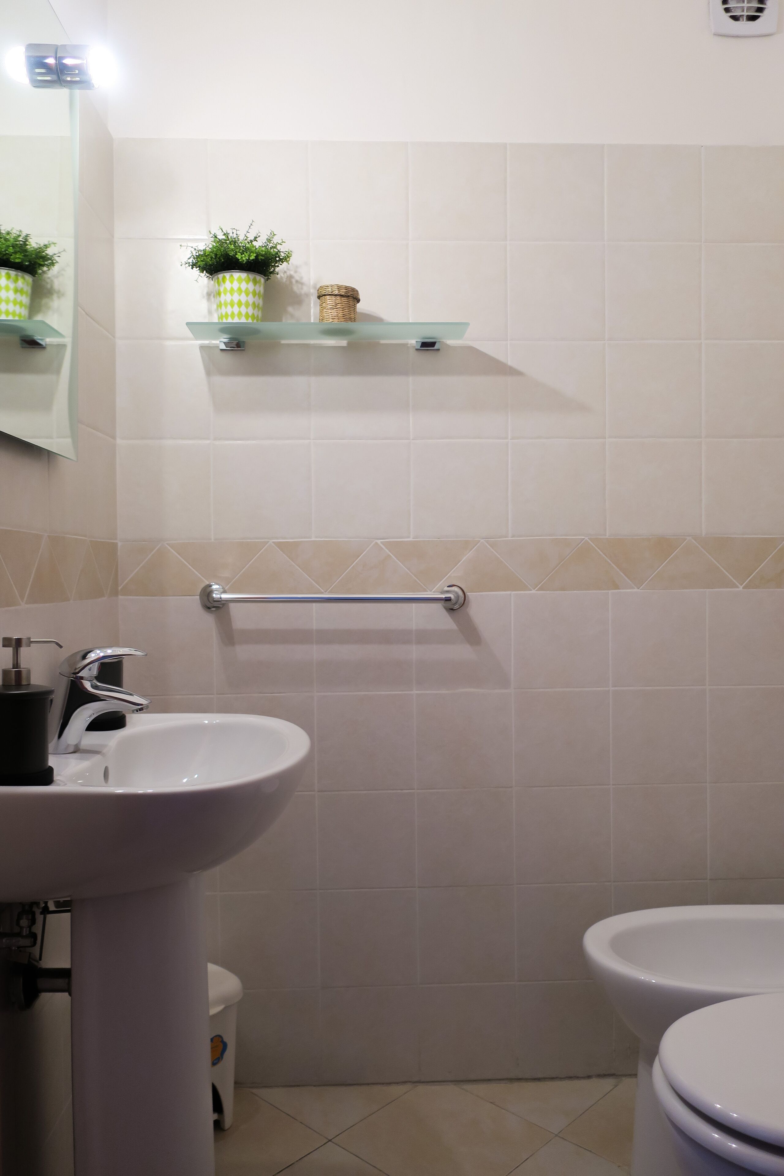 Un baño con un lavamanos blanco, un inodoro, un estante de vidrio con una planta y un perchero para toallas.