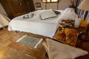 Un lit bien fait, avec un plateau contenant des aliments pour le petit-déjeuner, un panier de fruits et un croissant sur un autre plateau.