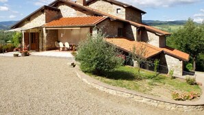 Una casa de piedra con techo de tejas, un porche cubierto con mobiliario exterior y un camino de grava.