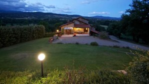 Una casa rústica con fachada de piedra, terraza de madera y césped bien cuidado.