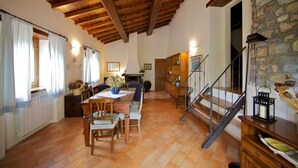 Un rincón comedor acogedor con una mesa y sillas de madera, una pared de piedra y una escalera que sube a otro nivel.