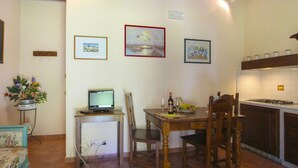 A dining area with a table, chairs, a TV, and a kitchen in the background.