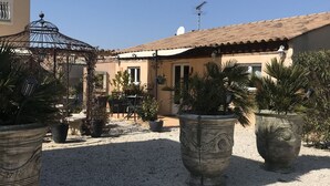 A courtyard with large planters, a pergola, and a building with a tiled roof. - L'Oasis - a little paradise in Provence, big terrace and pool (Arles)