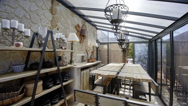 A covered patio with stone walls, a wooden table, and shelves with various items. - L'Oasis - a little paradise in Provence, big terrace and pool (Arles)