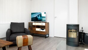 Un salon comprenant un canapé, un téléviseur, un meuble en bois, une petite table et un poêle à bois.