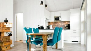Une cuisine moderne avec des meubles blancs, un pare-feu en pierre et une table à manger en bois, assortie de chaises de couleur turquoise.
