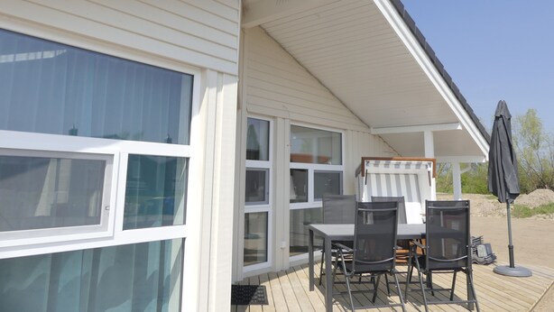 Une terrasse extérieure couverte, avec une table et des chaises, une fenêtre et une porte.
