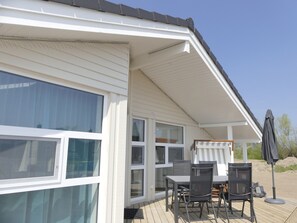 Enjoy outdoor dining or relaxation in this covered area with a wooden deck, featuring windows with clear glass and a comfortable seating area.