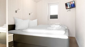 Une chambre moderne avec un grand lit, une table de chevet, un téléviseur fixé au mur et une fenêtre avec des stores.
