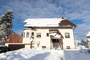 Una casa a due piani con tetto innevato e una scala che conduce all'ingresso.
