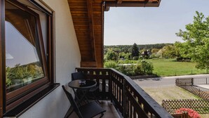 A balcony with a table and chairs, a view of a green landscape, and a wooden ceiling.