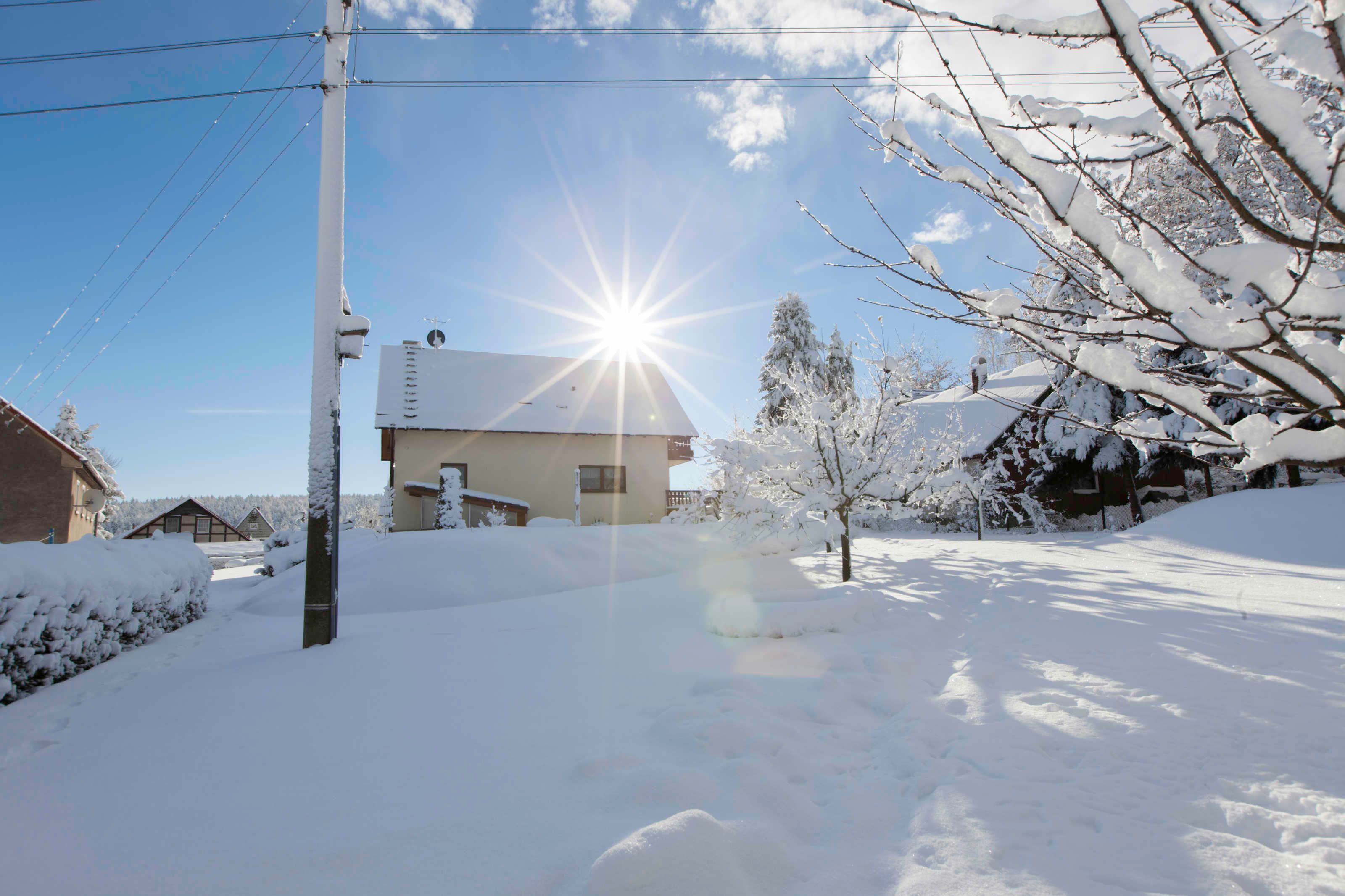 A residential area with a house, snow-covered trees, and a clear sky.