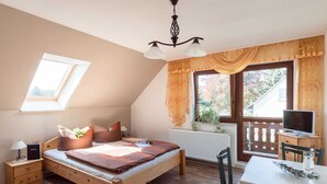 A bedroom with a wooden bed, a desk, a chair, a radiator, a window with curtains, and a TV.