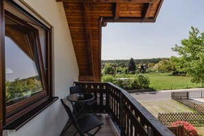 Een balkon met een tafel en stoelen, een uitzicht op een groen landschap en een houten plafond.
