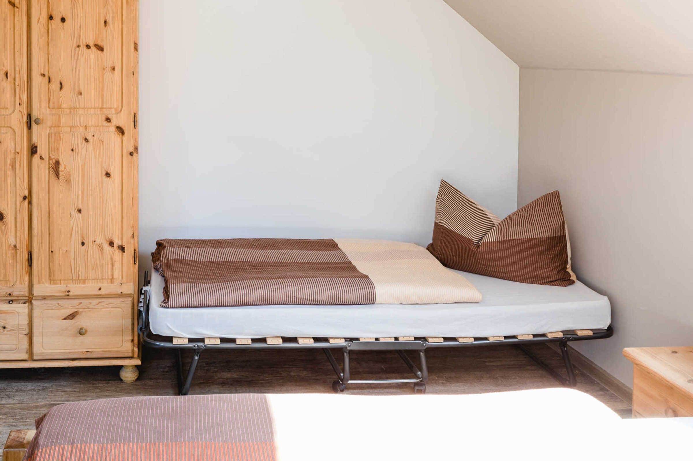 Un lit simple avec un cadre en métal, une armoire en bois et une petite table en bois.