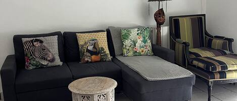 A living room with a black sofa, a round side table, a patterned throw pillow, a star-shaped wall decoration, and a lamp.