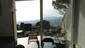 Ein Essbereich mit Tisch und Stühlen, einer Vase und Blick auf einen Garten sowie Hügel in der Ferne durch eine Glastür.