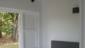A bedroom with a bed, patterned bedspread, and pillows. There is a window with a view of greenery outside.