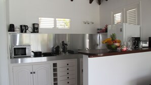 A modern kitchen with white cabinetry, a microwave, a coffee maker, and a fruit bowl on the counter.