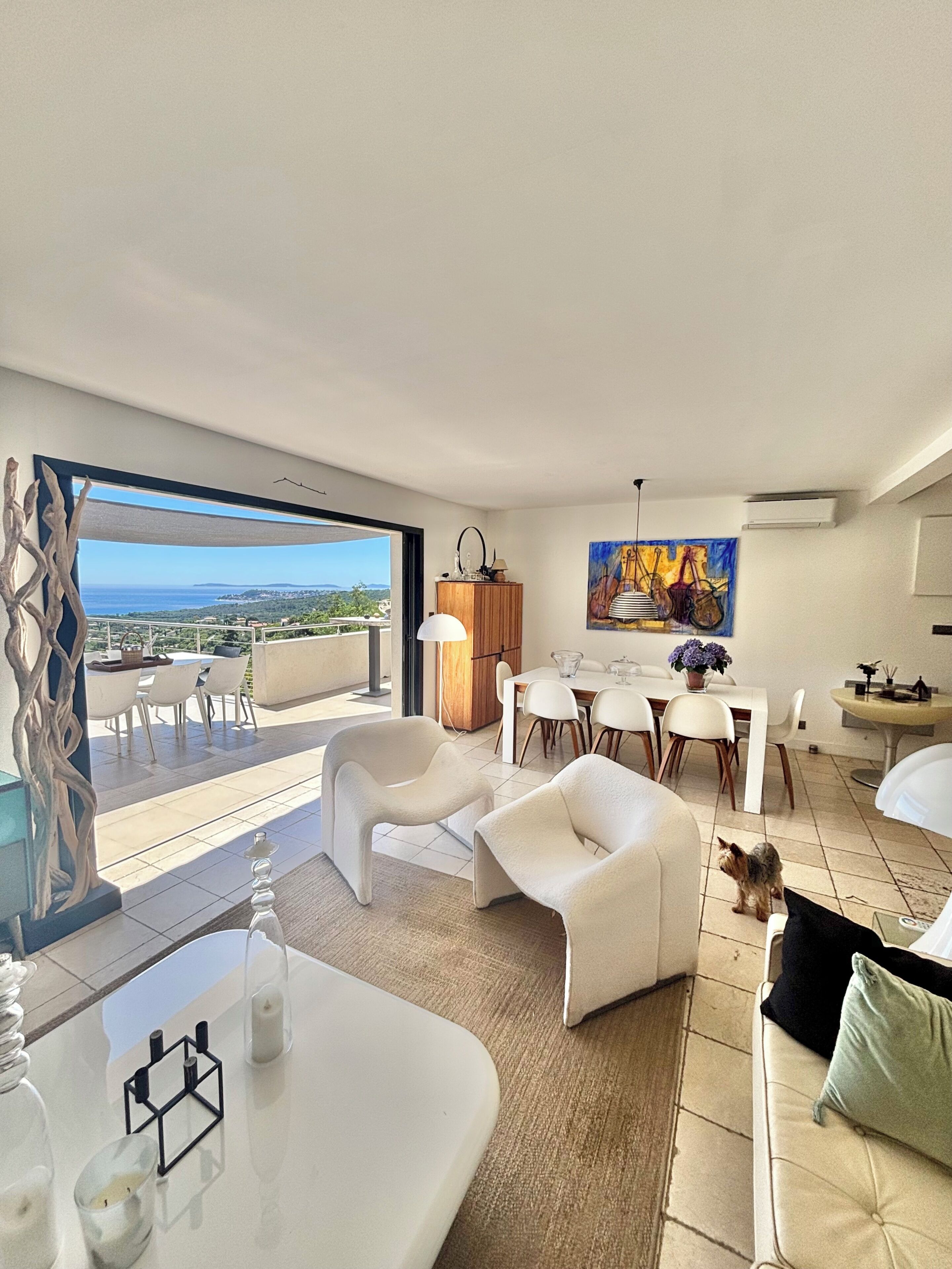 A modern living room with a dining area, a view of the sea, and a painting on the wall.