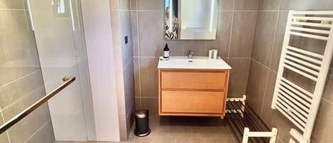 A modern bathroom with a shower, a sink, a mirror, and a towel rack.