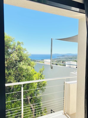 A balcony with a view of a body of water, greenery, and distant buildings.