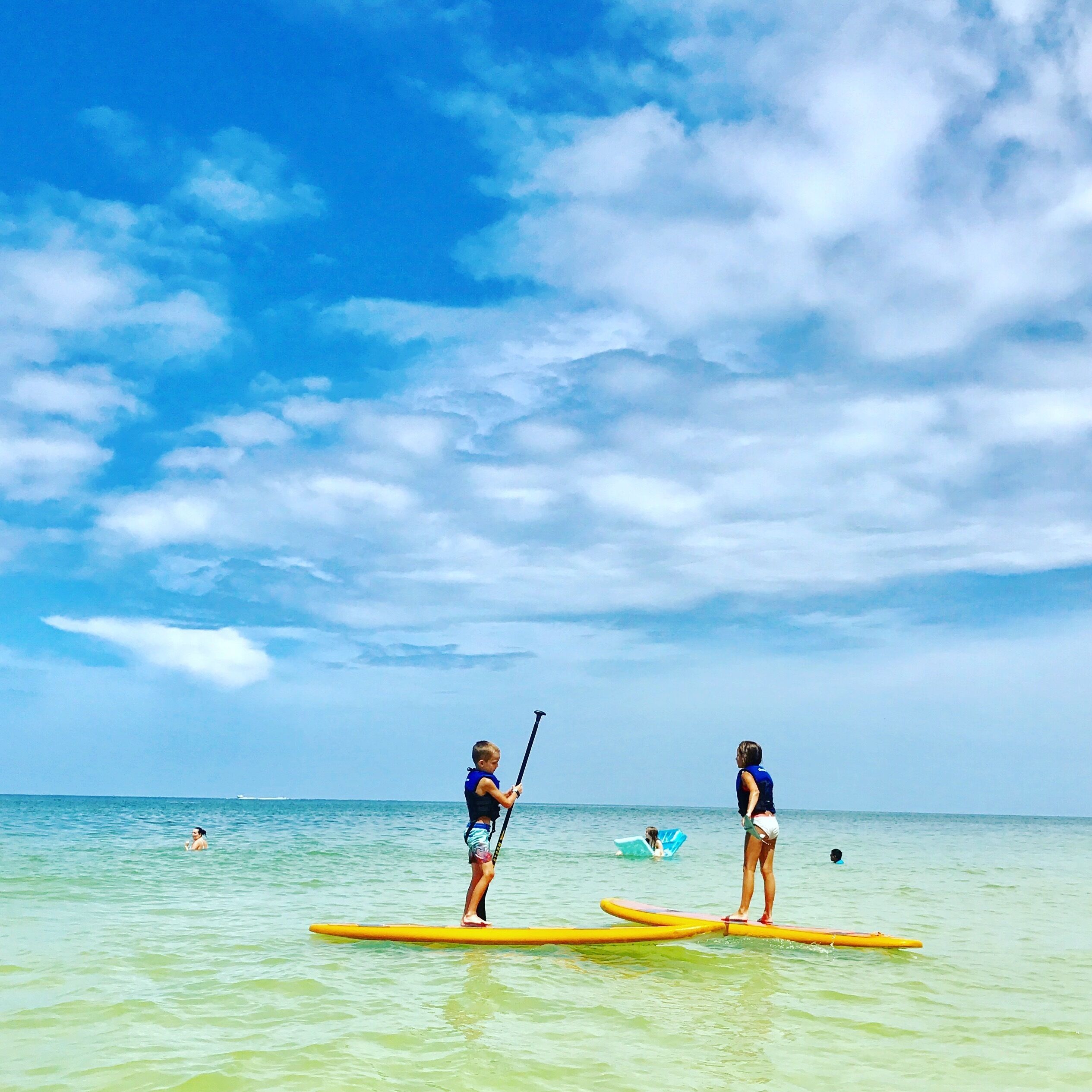 Dos personas en tablas de paddleboard sobre aguas tranquilas bajo un cielo despejado.