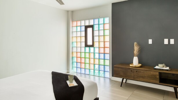 A modern bedroom with a bed, a ceiling fan, a wooden dresser, and a colorful stained glass window. - Eazy Centro by ULIV (Tijuana)