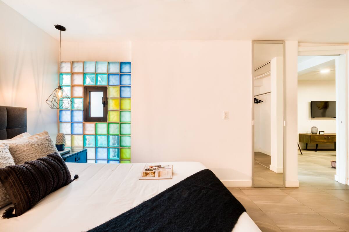 Un dormitorio con cama, mesita de noche, lámpara y pared con azulejos de colores.