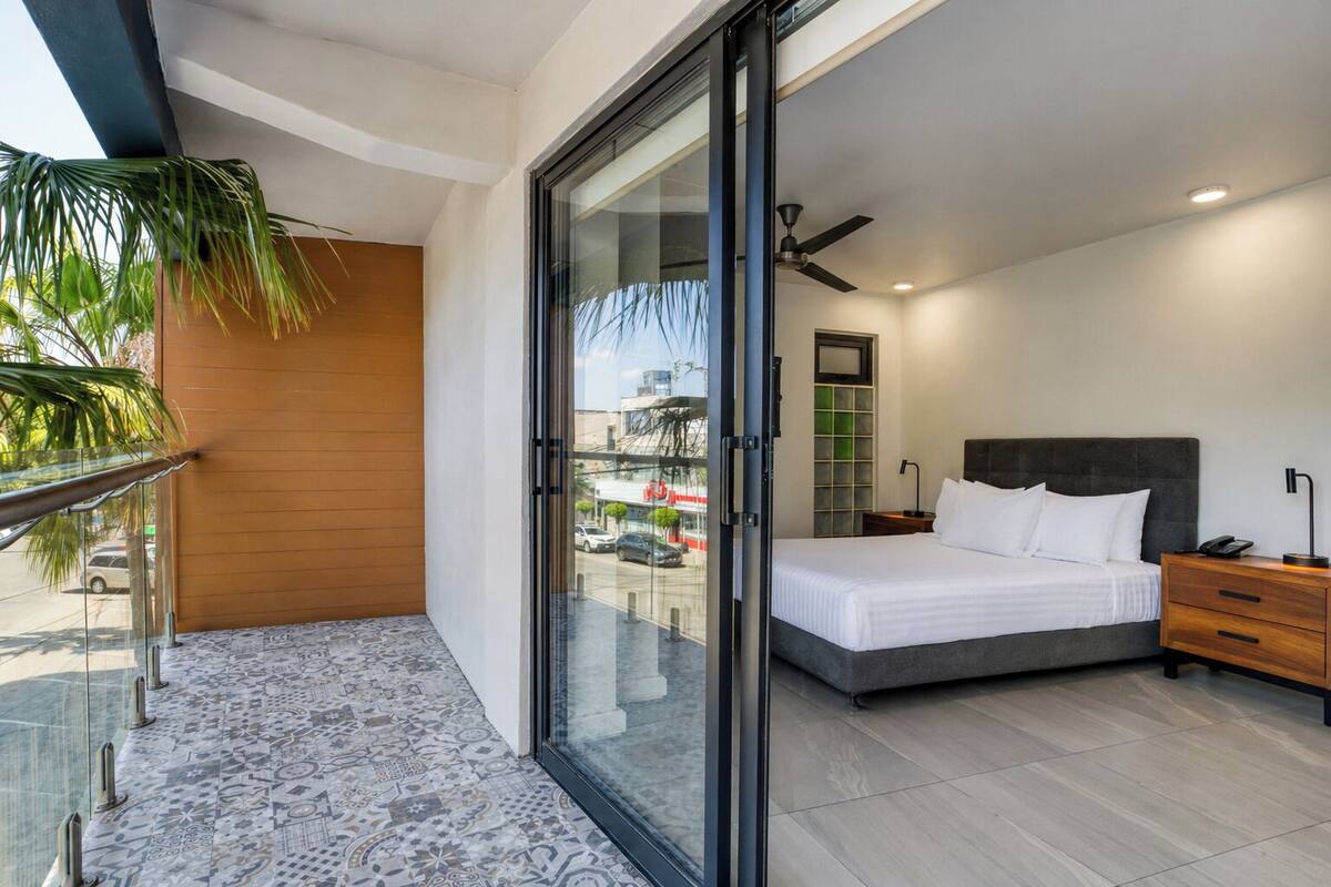 Habitación de hotel moderna con cama, mesita de noche y vista a través de un ventanal.