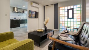 A modern living room with a sofa, coffee table, and a glass of wine. There is a kitchen in the background with a TV and an air conditioning unit. - Eazy Centro by ULIV (Tijuana)