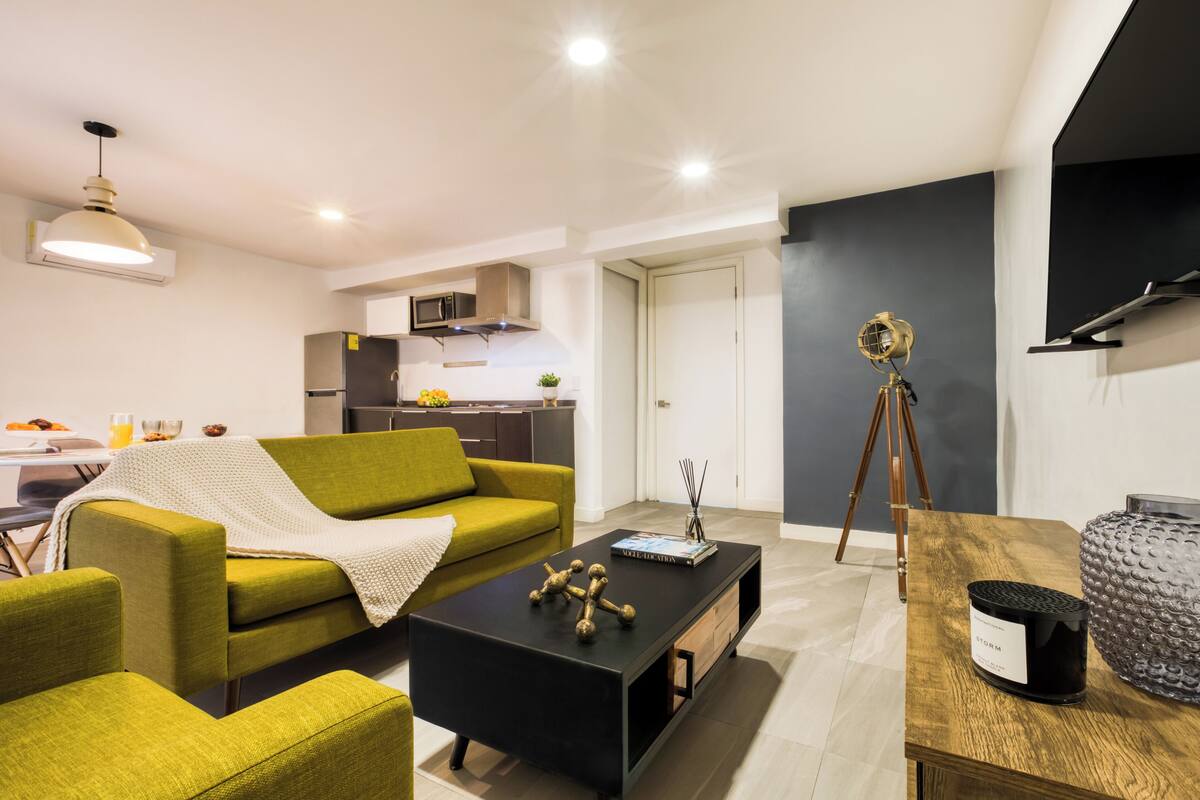 Una sala moderna con un sofá verde, una mesa de centro negra y un comedor con una mesa y sillas blancas.