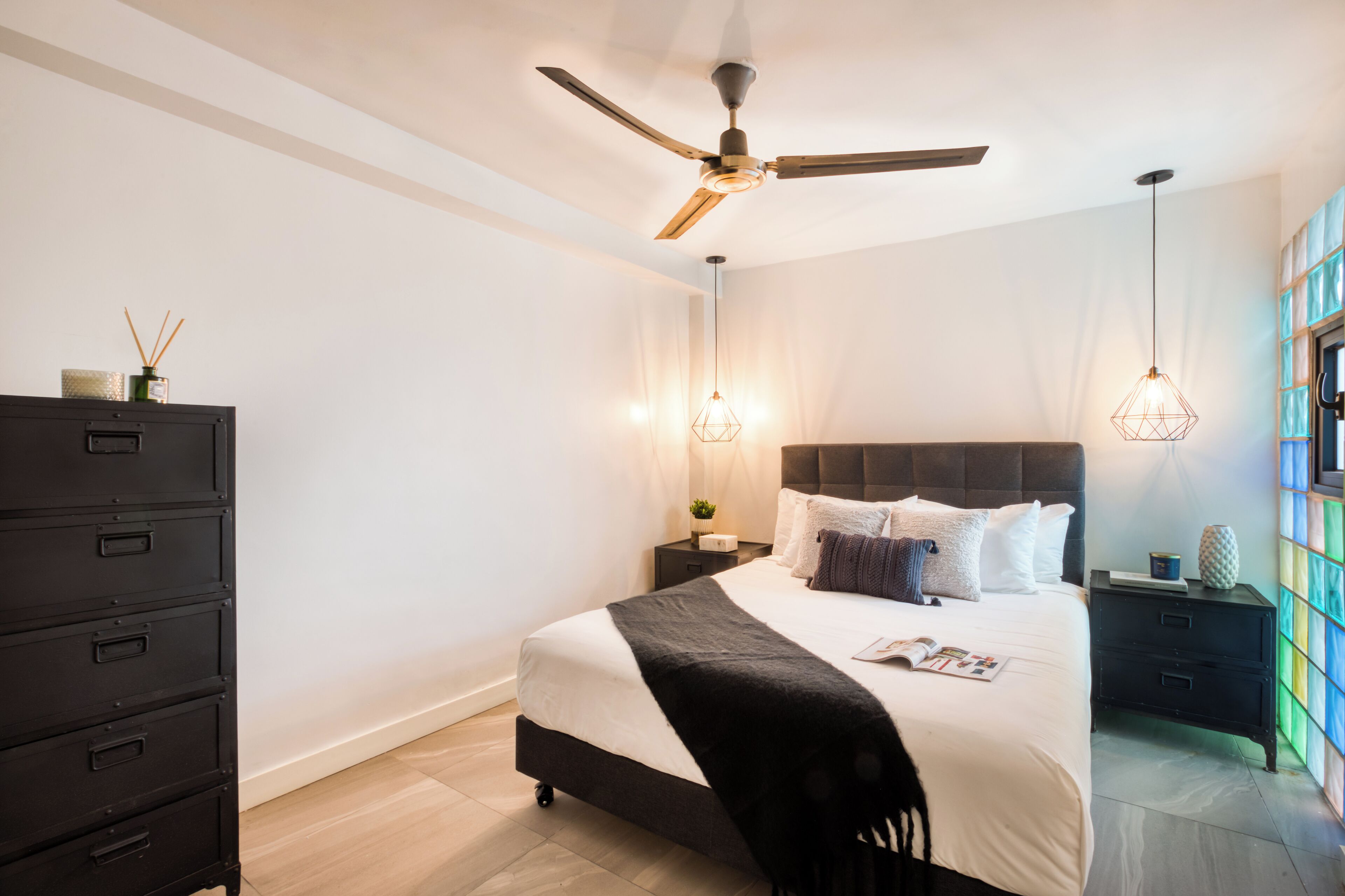 Un dormitorio moderno con cama, ventilador de techo, cómoda y mesita de noche con lámpara.