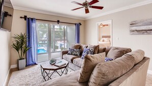 A living room with a beige sofa, a coffee table, a potted plant, and a ceiling fan.