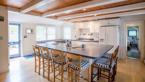 A spacious kitchen with a large island, wooden chairs, and white cabinets. - Ten min. walk to Main St. Perfect for families/groups. Gorgeous enclosed yard. (Nantucket)